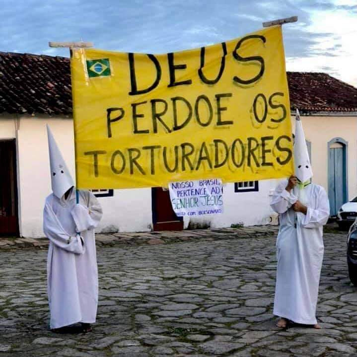 Manifestantes utilizando vestimenta de procissão do fogaréu, com cartaz pedindo para que "Deus perdoe os torturadores"